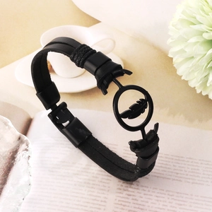 Punk style black leather bracelet with metal feather charm on a magazine background
