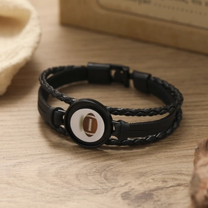 Detail of multi-layer black braided leather bracelet with american football charm