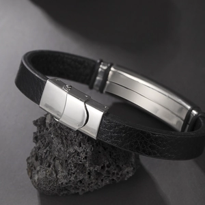 Minimalist men's black leather bracelet with polished silver metal clasp on dark rock