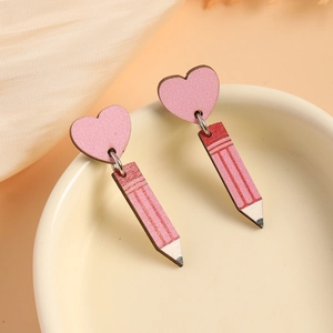 Pink heart and pencil wooden drop earrings displayed in a beige ceramic bowl