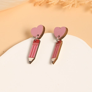 Detail of wooden heart and pencil earrings on a white stone base with pink backdrop