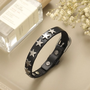 Bracelet punk en cuir noir avec clous étoiles argentés et boucle sur fond décoratif
