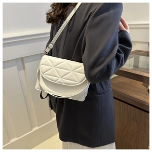 Close-up of a white quilted crossbody bag with adjustable strap on a dark blazer