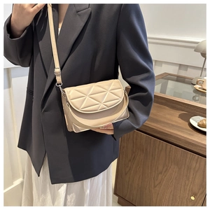 Detail of beige crossbody bag with triangular quilting worn with a navy blue blazer