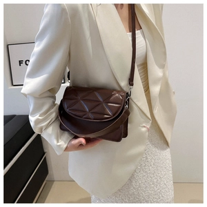 Detail of dark brown quilted crossbody bag with long strap shown on model in white suit