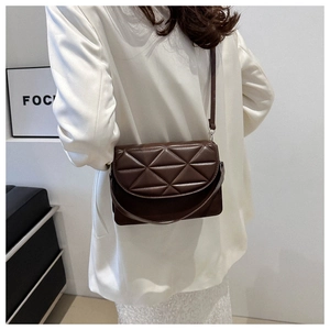 Detail of dark brown quilted crossbody bag with adjustable strap on white suit model