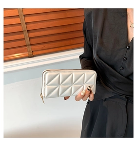 Detail of white quilted leather long wallet with gold zipper held by a model