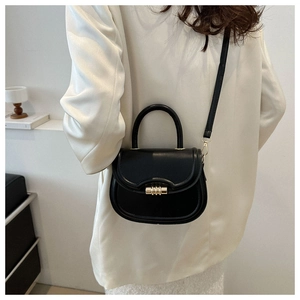 Detail of black leather saddle bag featuring a gold cylindrical lock and top handle