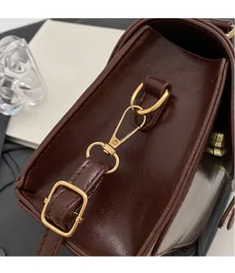 Detailed close-up of the golden metal hardware and detachable strap on a brown PU bag