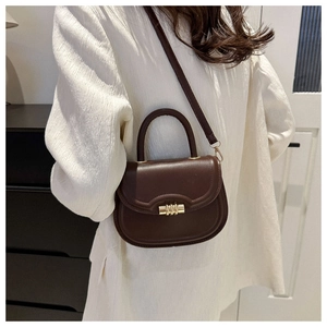 Detail of vintage dark brown saddle bag with gold metal clasp on a textured white shirt