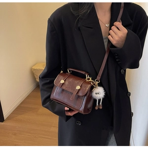 Detail of a brown leather crossbody square bag with gold buckle and white plush charm