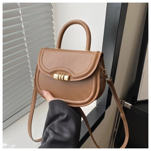 Detail of tan leather saddle bag with gold cylindrical buckle and top handle
