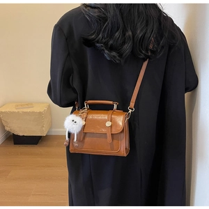 Detail of a brown vintage leather crossbody bag featuring a playful white plush monster charm
