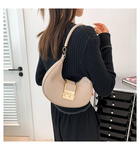 Detail of minimalist beige crescent shoulder bag featuring a prominent gold metal buckle