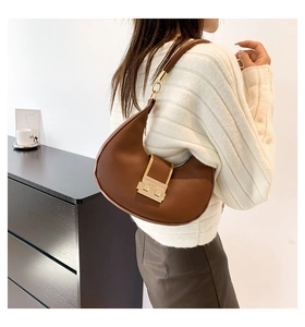 Brown leather crescent underarm bag with a gold buckle shown on a model's shoulder