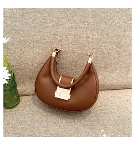 Detailed view of brown leather crescent bag with golden metal buckle and thick handle
