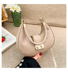 Close-up of beige crescent moon bag featuring a gold round handle and square metal buckle