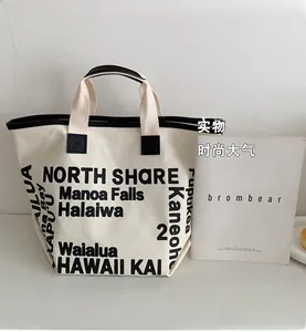 Detailed close-up of large canvas tote bag with black letter print and leather handle trim