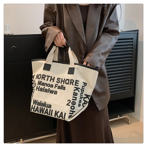Détail d'un grand sac cabas en toile avec garniture noire porté par un mannequin chic