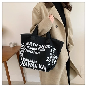 Vue détaillée du grand sac cabas noir en toile avec lettrage blanc porté par un mannequin