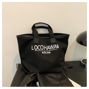 Detail of reinforced stitching and white letter printing on a black canvas tote bag