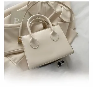 Detail view of cream crossbody square bag next to a smartphone for size scale
