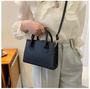Detail view of a black minimalist leather crossbody bag worn by a model in a cozy room