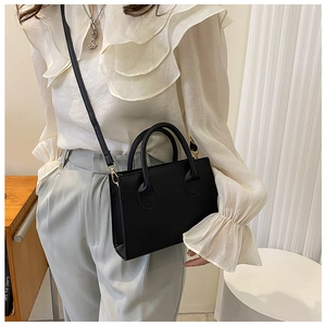 Sac bandoulière rectangulaire minimaliste en cuir mat noir porté par un modèle
