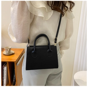 Détail d'un sac carré noir minimaliste avec poignées rondes et boucles dorées ajustables