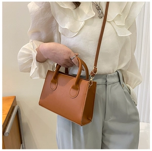 Detail of a brown leather crossbody bag with top handles and gold metal hardware hooks