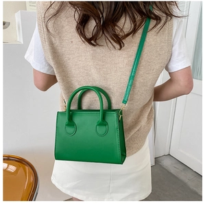 Detail of green square crossbody bag with round top handles and gold hardware
