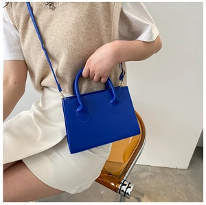 Chic bright blue square handbag with top handles and shoulder strap shown on a model