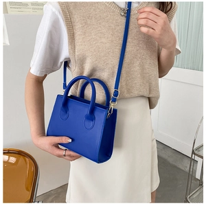 Detail view of Klein blue square crossbody bag with cylindrical handles and golden hardware