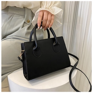 Detail of a black matte faux leather handbag with golden metal clasps and round handle