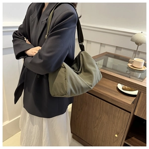 Olive green nylon dumpling bag styled on a person with a wide black shoulder strap