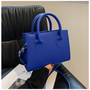 Detail of blue square crossbody bag with gold hardware and stylish round handle