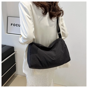 Side view of a black minimalist nylon crossbody bag worn by a model in a modern room