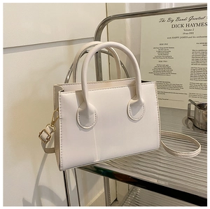 Detail of a minimalist cream-colored crossbody bag with stitching and golden hardware