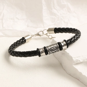 Detalle de pulsera de cuero trenzado negro con cuenta étnica plateada y cierre ajustable