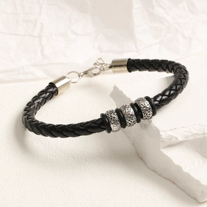 Detalle de pulsera de cuero trenzado negro con cuentas plateadas y cierre de mosquetón