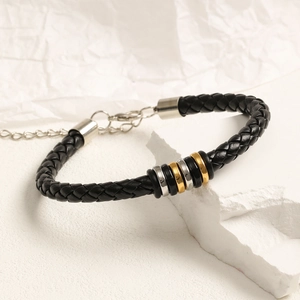 Detalle de una pulsera de cuero trenzado negro con anillos de metal plateado y dorado