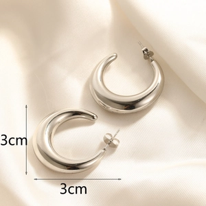 Macro shot of 3cm silver stainless steel C-shaped hoop earrings on white silk fabric