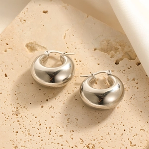 Close-up of polished silver hoop earrings on stone surface with silk fabric detail