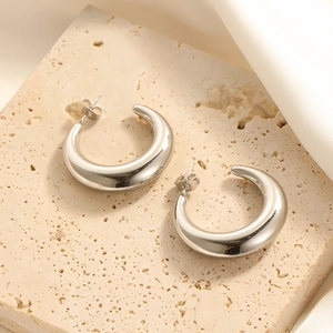 Close-up of chunky silver stainless steel hoop earrings on natural stone with soft fabric