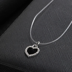 Detalle del collar con colgante de corazón negro con pedrería e hilo de pescar invisible