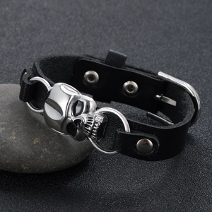 Gothic leather bracelet with silver skull charm on stone background, punk style jewelry