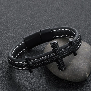 Detail of woven black leather bracelet with metal cross and magnetic clasp on a stone