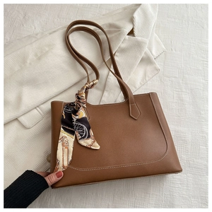 Detail of vintage brown tote bag featuring white stitching and elegant silk scarf handle