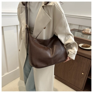Close-up of vintage brown textured leather tote bag worn with a light trench coat