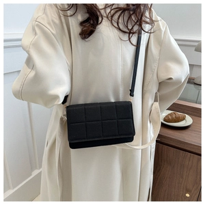 Detalle de un bolso bandolera acolchado negro con herrajes dorados usado por un modelo